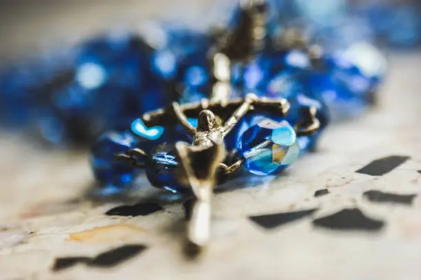 Photo of closeup of a metal cross with jesus blue glass rosary convoluted