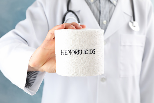 Doctor holds toilet paper with Hemorrhoids on blue background, close up