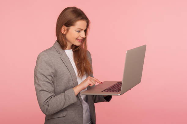 Portrait of smart office employee typing on laptop, elegant positive businesswoman in suit jacket using computer Portrait of smart office employee typing on laptop, elegant positive businesswoman in suit jacket using computer to study, working online, doing job remotely. studio shot isolated on pink background smart office stock pictures, royalty-free photos & images