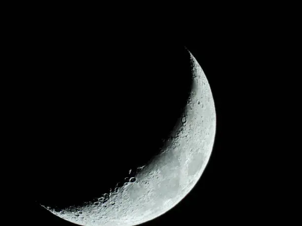 the increasing sickle-shaped quarter moon with its moon craters stands in the black night sky