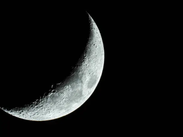 the increasing sickle-shaped quarter moon with its moon craters stands in the black night sky