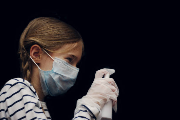 a young girl in a medical mask and gloves sprays antiseptic in an aerosol on viruses. isolate on a black background. the concept of taking preventive measures to protect against disease. - flu virus russian influenza swine flu virus imagens e fotografias de stock