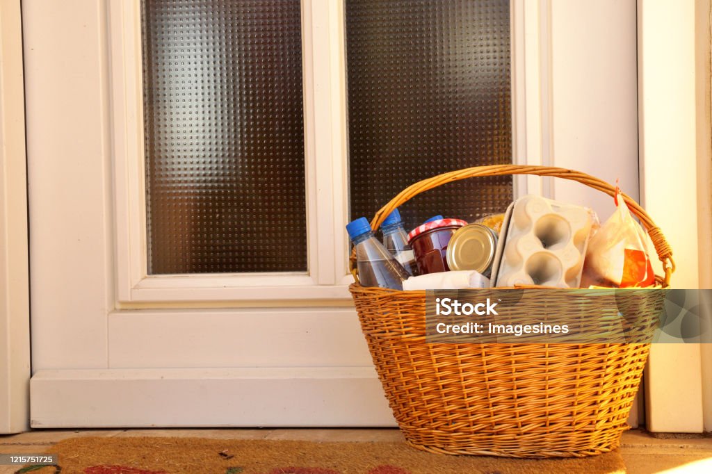 delivery during the quarantine. full willow wicker basket with Merchandise, goods and food in front of the door, neighborhood Assistance concept at quarantine time  of coronavirus infection Covid-19 Food delivery concept. neighborhood Assistance during Coronavirus Pandemic - Illness, solidarity Basket Stock Photo