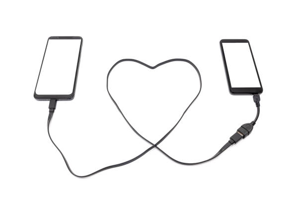 Hand connecting two smartphones with a heart shaped USB cable. Long distance relationship concept.