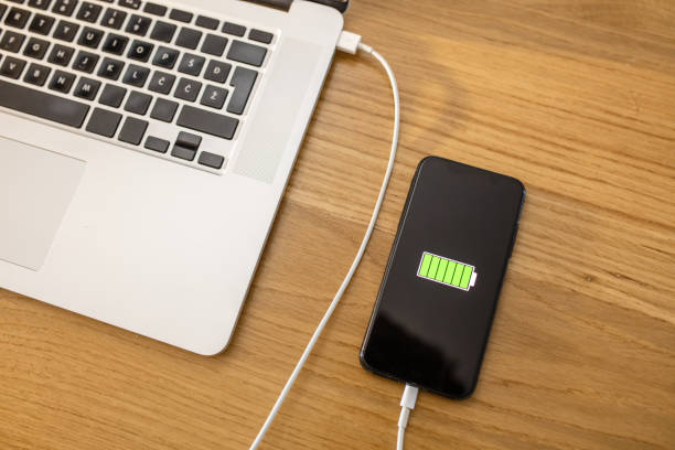 istock Smart phone with USB cable charging at laptop 1215755906