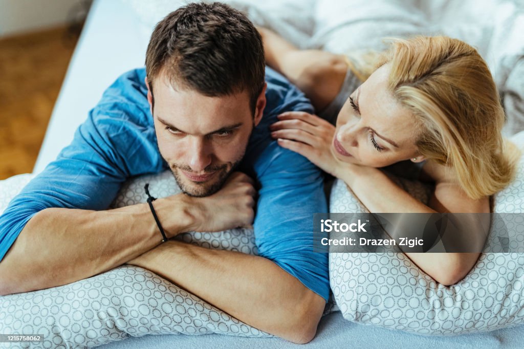 Young displeased couple with relationship difficulties in bedroom. Young couple lying down on bed while having problems in their relationship. Couple - Relationship Stock Photo