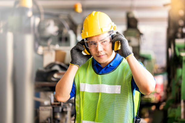 professionelle techniker tragen schutzausrüstung und harthüte in großen industrieanlagen. schutz- und sicherheitsausrüstung augenbekleidung, ohrstöpsel, vis-kleidung und schutzhelm. - protection stock-fotos und bilder