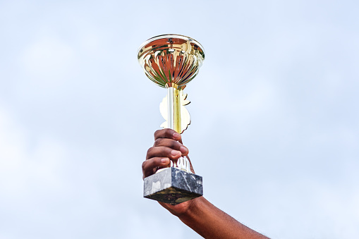 Cropped shot of an unrecognizable person holding up a trophy in the air outside during the day