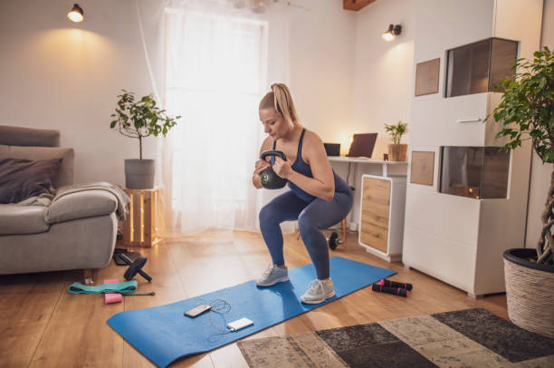 jeune femme s’accroupi avec kettlebell sur le tapis de yoga dans le salon - home fitness photos et images de collection