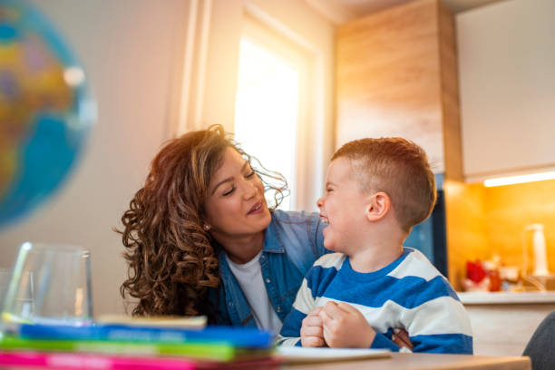 Kind mother helping her son doing homework in kitchen. Kind mother helping her son doing homework in kitchen. Mother Helping Son With Homework At Table. Children's creativity. Portrait of smiling mother helping son with homework in kitchen at home developmental disability stock pictures, royalty-free photos & images