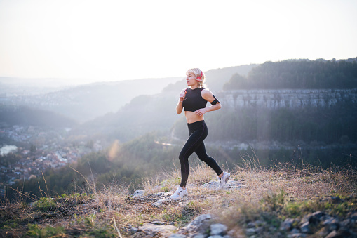 Young woman trail running on the top of hill over the city.