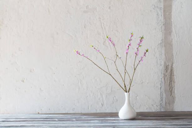 istock daphne flowers in vase on old wooden table on background white wall 1215765538