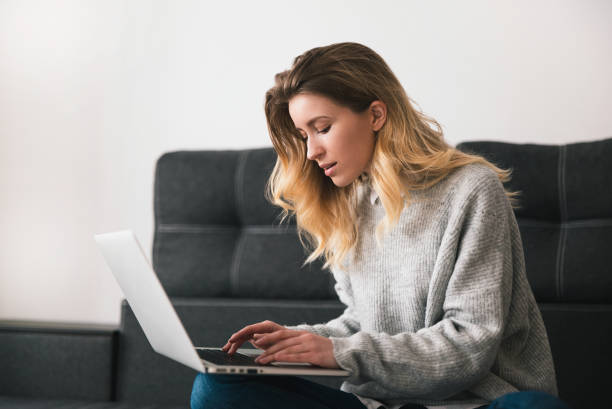 istock young blond beautiful woman sits on the sofa working from home on her laptop during quarantine, cozy home atmosphere concept 1215766653
