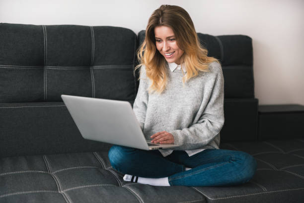 istock young blond smiling woman sits on the sofa working from home on her laptop during quarantine, cozy home atmosphere concept 1215766655