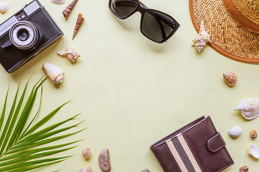 Men's traveler accessories: green tropical palm leaf, photo camera, seashells and sunglasses are on yellow background with copy-space. Top view travel or vacation concept, flat lay summer background