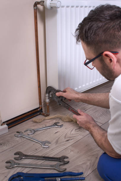 istock Plumber holds the adjustable wrench and adjusts the tool spacing. Unscrewing the connection screw from the radiator. The flat keys and tow are on the floor. 1215769882