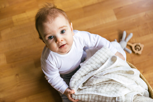 A eight-month-old baby crawls on the floor, looks down at the camera. Domestic affairs with a child, what to do with a baby