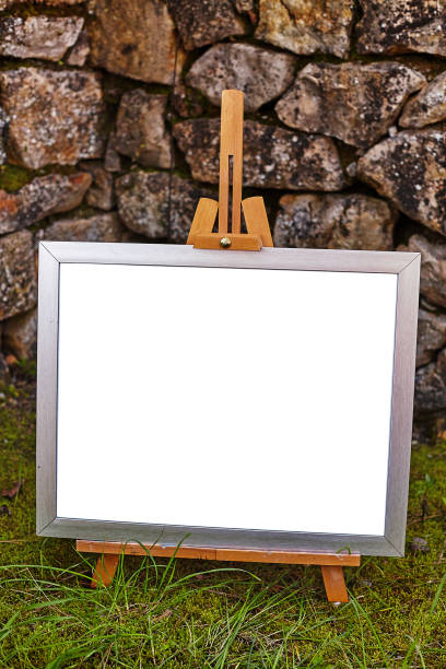 istock Easel staying om grass and moss near ancient stone walll with copy space 1215772031