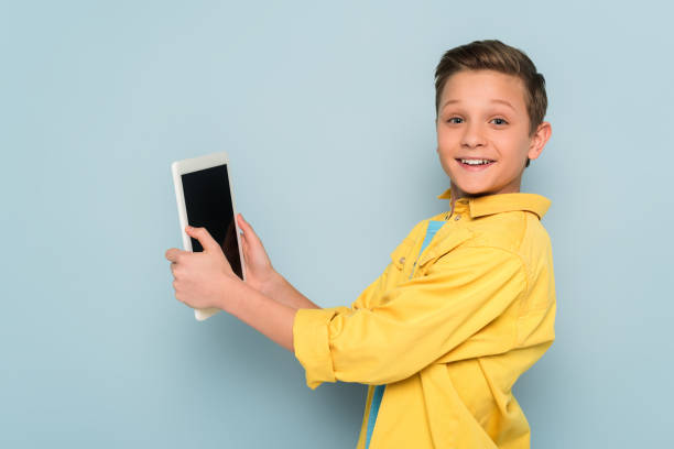 smiling kid holding digital tablet and looking at camera on blue background