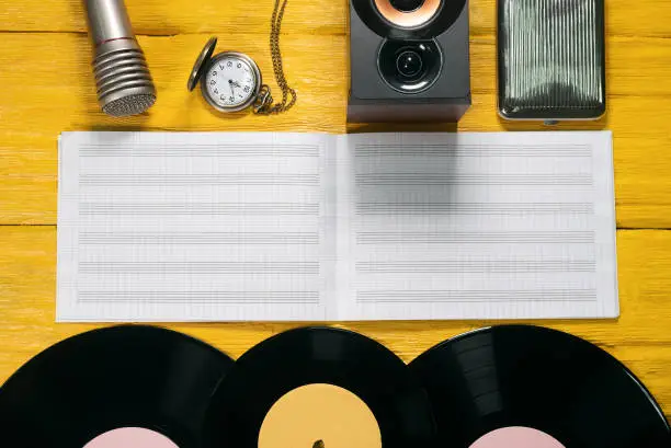Retro vinyl record, music book, microphone and speakers on yellow flat lay background.