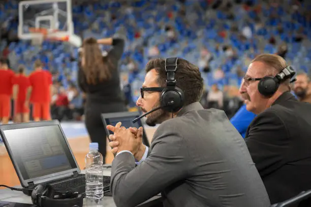 Basketball commentators wearing headphones using laptops in Arena Stozice, Ljubljana, Slovenia.