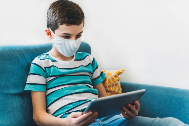 istock Cute boy with face protective mask studying at home. Online education. Coronavirus epidemic 1215778550
