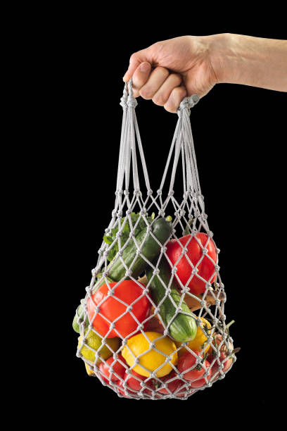 istock Shopping bag mesh with healthy vegetables on a black isolated background. Zero waste. Man's hand holding bag with mesh products. 1215779649