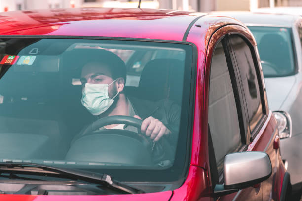 homme avec le masque protecteur assis dans la voiture dans l’embouteillage et regardant vers l’avant
 - covid-19 corona crisis concept picture - traffic jam traffic car city photos et images de collection