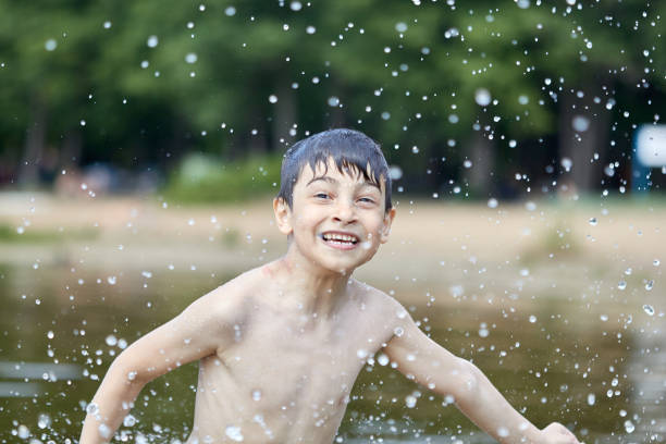 istock Boy splashes in lake flying splashes of water 1215783140