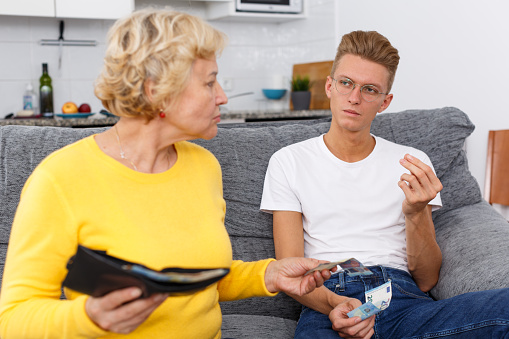 Senior woman giving money her adult son at kitchen