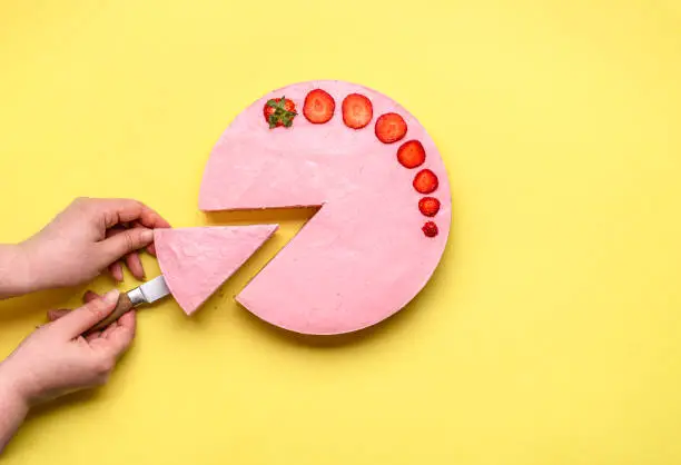Woman slicing a strawberry cheesecake slice, on a yellow seamless background. Serving a no-bake cheese cake with red berries. Summer fruity pie.