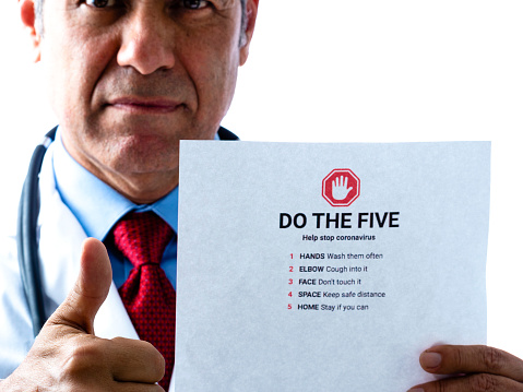 Doctor giving us the thumbs up that if you follow the five guidelines on the paper we can help stop the Covid-19 coronavirus. White background. Doctor in dramatic lighting