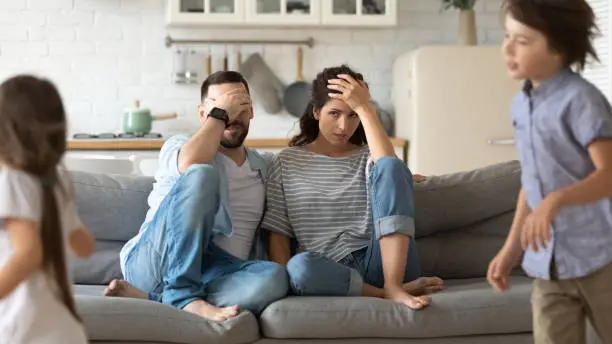 Photo of Tired young parents exhausted from loud kids playing