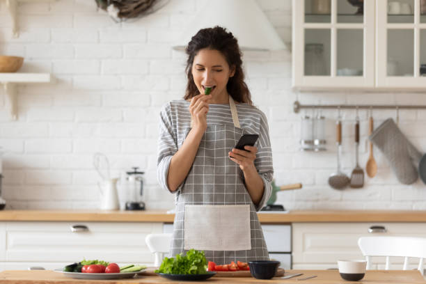 istock Smiling young woman cooking in kitchen using cell 1215789574
