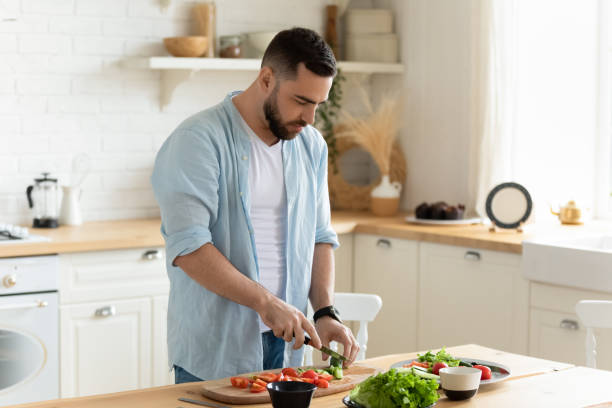 молодой человек стоит на кухне приготовления салата на обед - vegetable men cutting adult стоковые фото и изображения