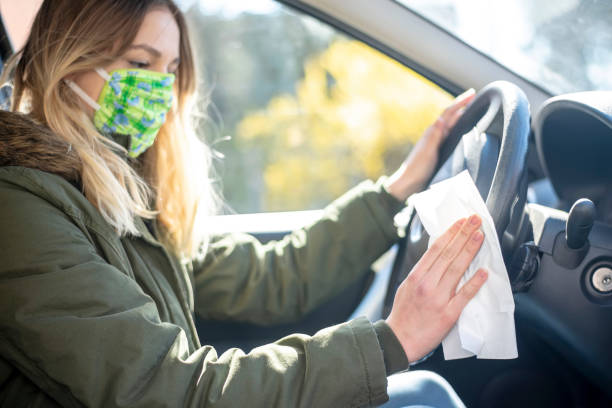 woman in car disinfecting steering wheel - illness mask pollution car imagens e fotografias de stock