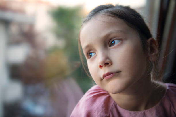 istock Little girl looking through window 1215790938