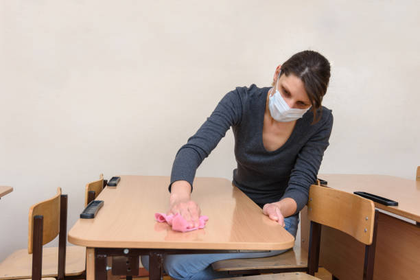 Girl in a medical mask washes tables in a school class during the quarantine period stock photo