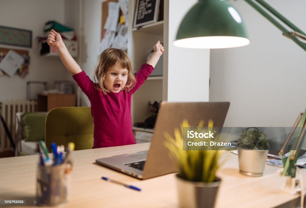 Ecstatic three year old girl celebrating winning on video game on laptop Cute three year old girl staying at home during COVID-19 lockdown and exploring new content on internet Child Stock Photo