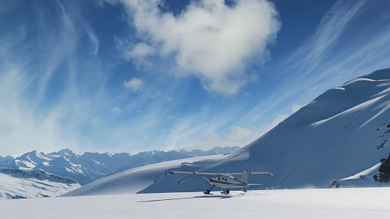 Small plane taking off from a snow field in Alaskan mountains with blue sky and clouds.
