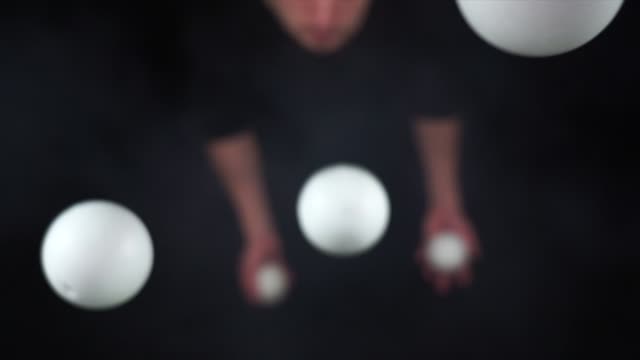 Circus artist wearing black juggling with white balls in slow motion
