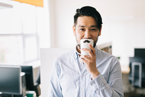 Young Asian man holding a coffee cup in front of his face