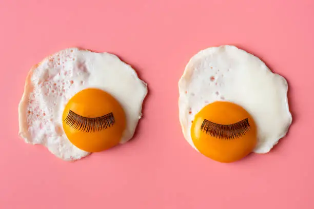 Pop art background. fried eggs with eyelashes on a pinkbackground. Food art. Morning concept. looks like eyes