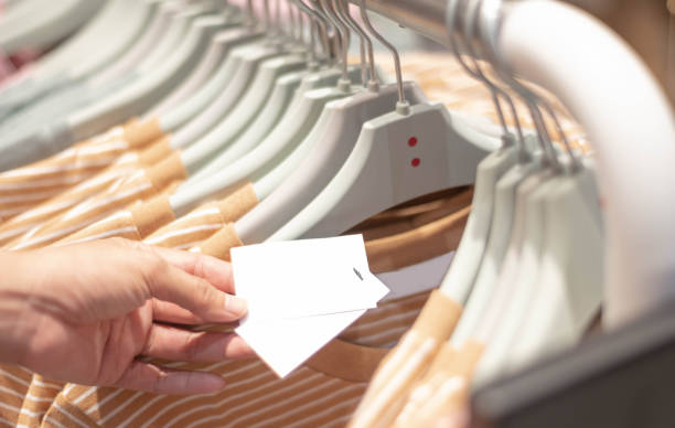 Hand holding blank paper price tag of checked pattern cotton shirt on the rack in cloth shop at department store. stock photo