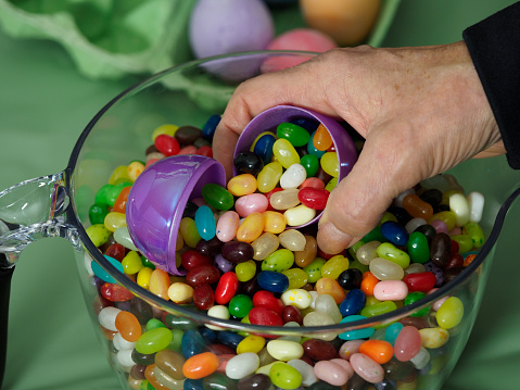 Plastic Easter Eggs filled with jellybeans to be used for a kids Easter egg hunt. Held in senior woman’s hand. Edited.