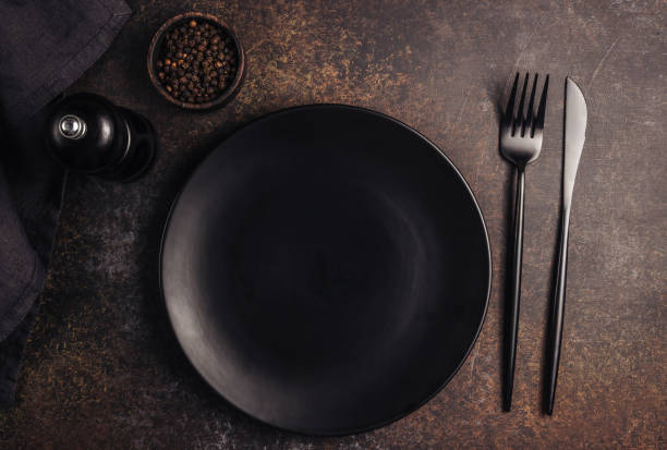 istock Elegant black table setting: plate, napkin and silverware over dark background. Flat lay. Top view. 1215819438