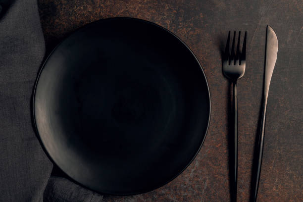 istock Elegant black table setting: plate, napkin and silverware over dark background. Flat lay. Top view. 1215819453