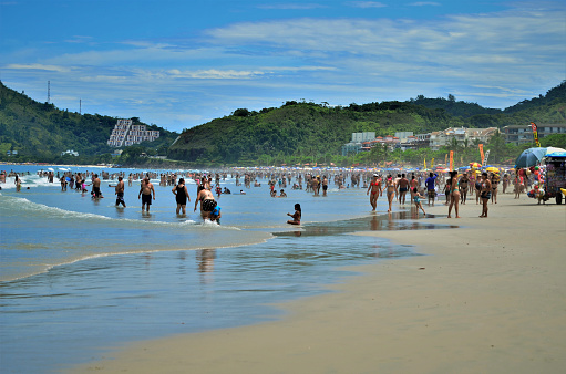 Large crowd of people on Bondi Beach in the Eastern Suburbs of Sydney on 2 January 2023.  The red and yellow coloured uniforms and surfboards of surf lifesavers are visible in the crowd, as is their yellow and red tent. The red and yellow flags indicate the area where it is safe to swim.  This image was taken at the northern end of the beach in the early afternoon.