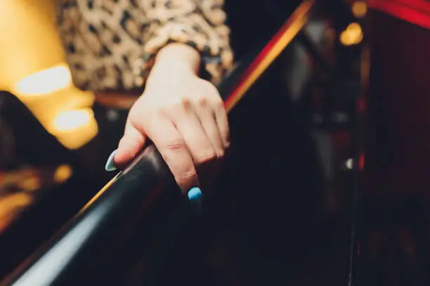 Photo of Woman hand using a railing to go upstairs with a light grey background.