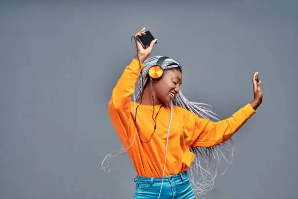 Photo of People, life, energy and music concept. Glad woman rejoices something, enjoys nice sound in new headphones, uses smartphone, listens song from playlist, spends time for dancing and entertaining
